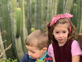 Portrait of cute girl with brother standing against cactus plants