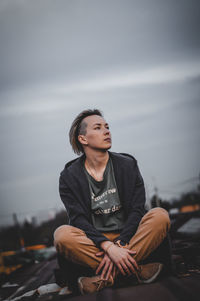 Young woman looking away while sitting against sky