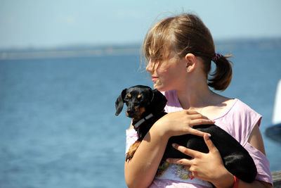 Girl carrying dachshund against sea