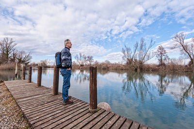 Man standing on pier over lake against sky