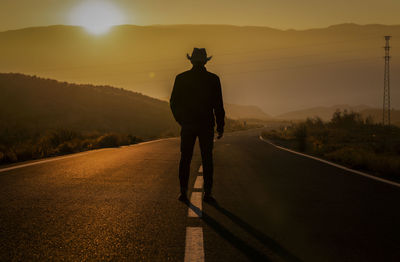 Silhouette of adult man in cowboy hat standing on country road during sunset. almeria, spain