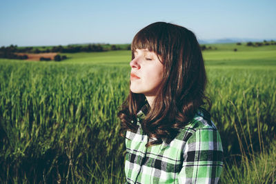 Woman with eyes closed standing on field during sunny day