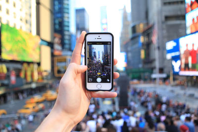 Cropped image of hand holding mobile phone in city