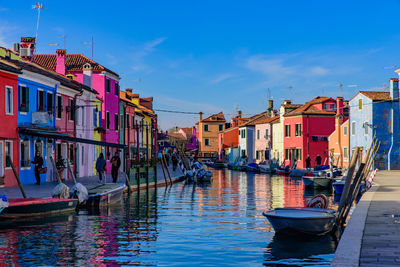 Boats moored in canal by buildings against sky in city