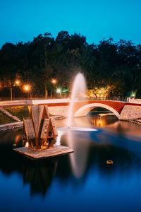 Illuminated arch bridge over river against sky at night