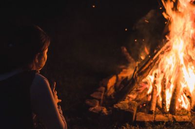 Side view of teenage girl sitting by campfire at night