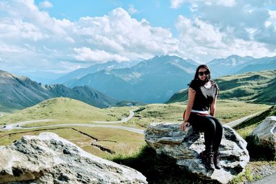 Young woman sitting on mountain against sky