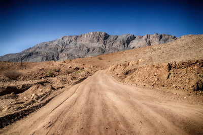 Dirt road in desert against clear sky