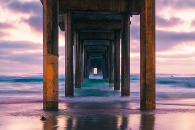 Below view of pier on sea shore against sky during sunset