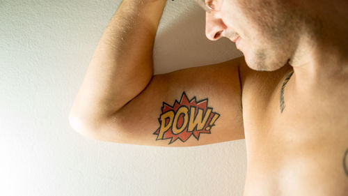 Midsection of man with tattoo on arm against wall