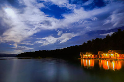 Lake by illuminated building against sky at night