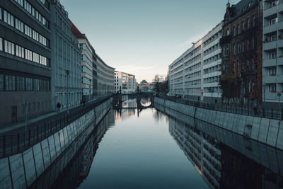 Canal in city against sky