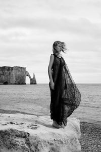 Young woman standing on rock at beach against sky