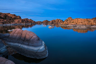 Reflection of rocks in lake against blue sky