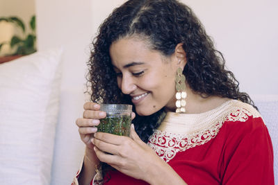 Smiling young woman holding drink at home
