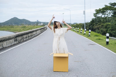 Woman with umbrella on road against sky