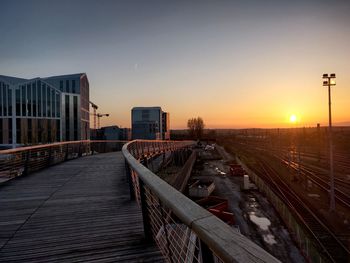 Railroad tracks by buildings against sky during sunset