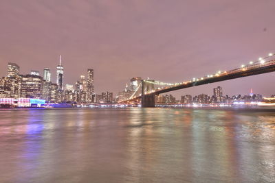 Illuminated bridge over river against buildings at night