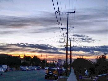 Cars on electricity pylon against sky during sunset
