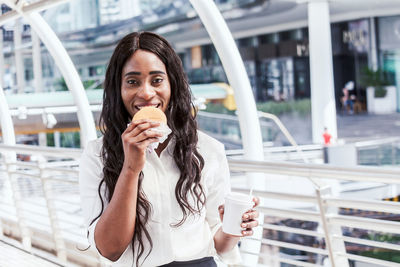 Businesswoman having food while standing in covered footbridge