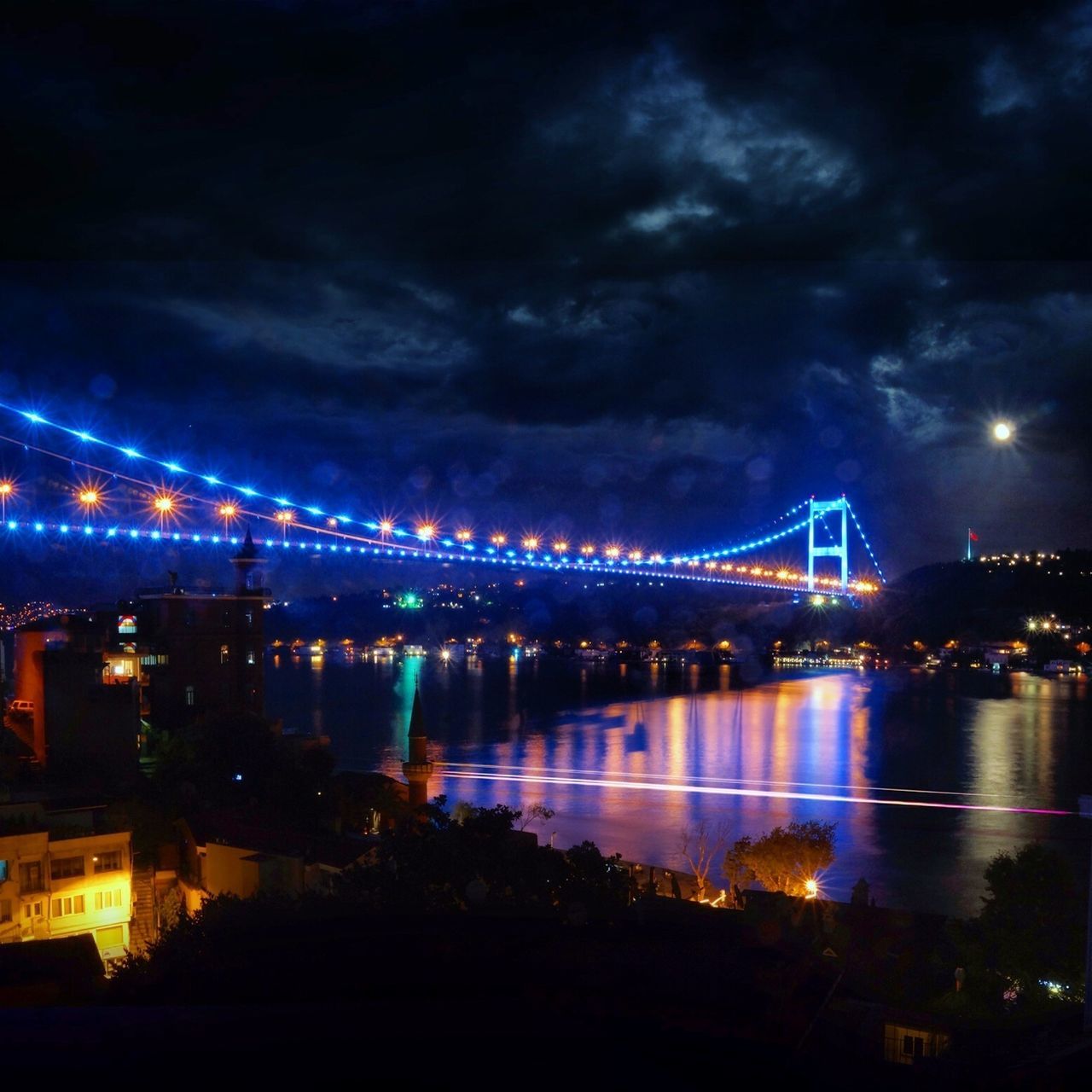 illuminated, night, connection, architecture, bridge - man made structure, built structure, sky, river, water, engineering, city, suspension bridge, bridge, cityscape, travel destinations, transportation, cloud - sky, building exterior, waterfront, famous place