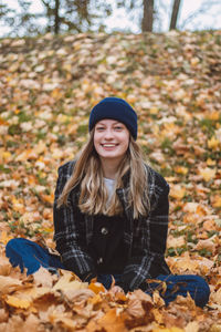 Smiling brunette sitting in a pile of colourful leaves in an oak forest throwing leaves