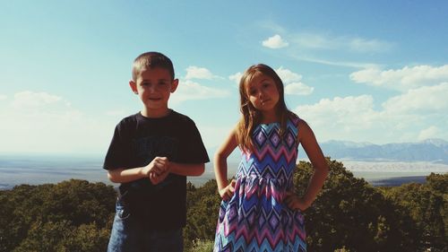 Portrait of smiling sibling standing against sky