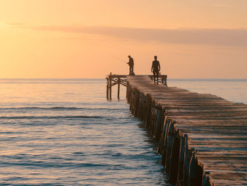 Man and woman on pier over sea against sky during sunset