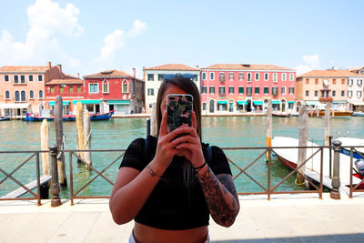 Full length of young woman photographing against sky