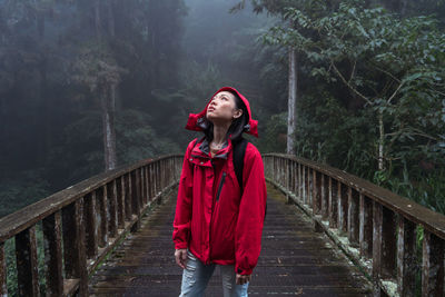 Woman standing on footbridge against trees