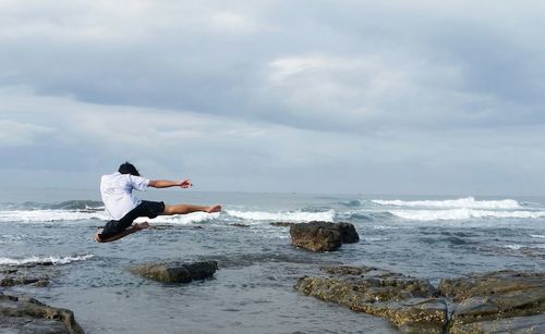 People on rock in sea against sky