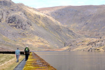 Rear view of people walking on mountain by lake