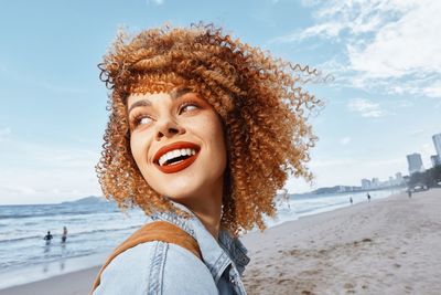 Young woman standing at beach against sky