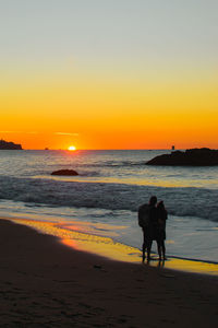 Silhouette people walking at beach during sunset