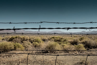 Barbed wire fence on field against clear sky