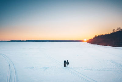 People on snow covered land against sky during sunset