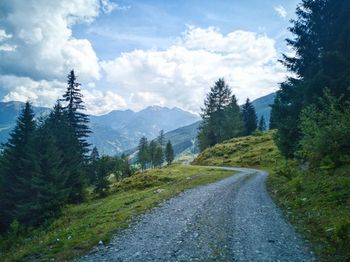 Road amidst trees and mountains against sky