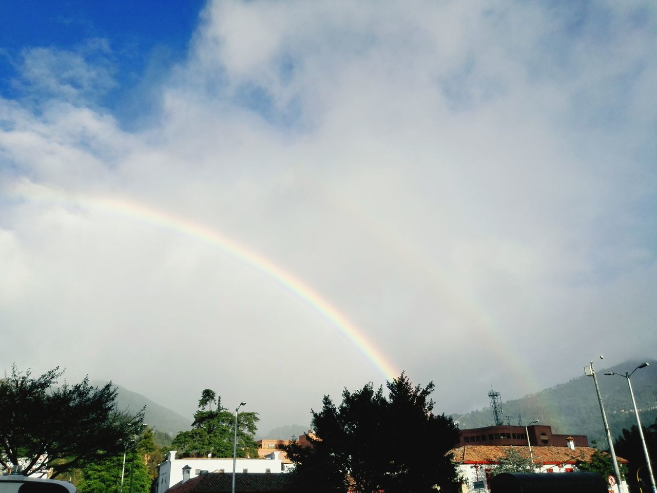 rainbow, sky, tree, cloud - sky, building exterior, built structure, architecture, low angle view, cloudy, multi colored, weather, house, nature, beauty in nature, cloud, scenics, outdoors, storm cloud, no people, blue