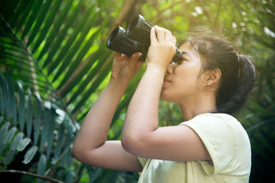 Young woman looking thorough binoculars in forest