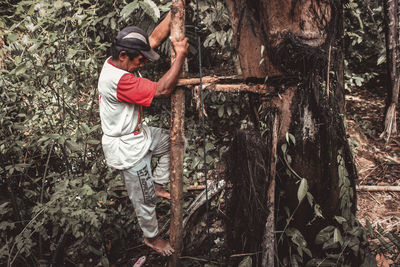 Full length of man holding tree trunk in forest