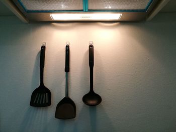 Spatulas and serving spoon hanging on wall under illuminated ventilation hood