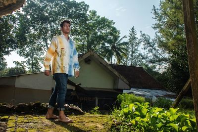 Young man standing barefoot at the backyard of a house in kemantren village, malang regency.