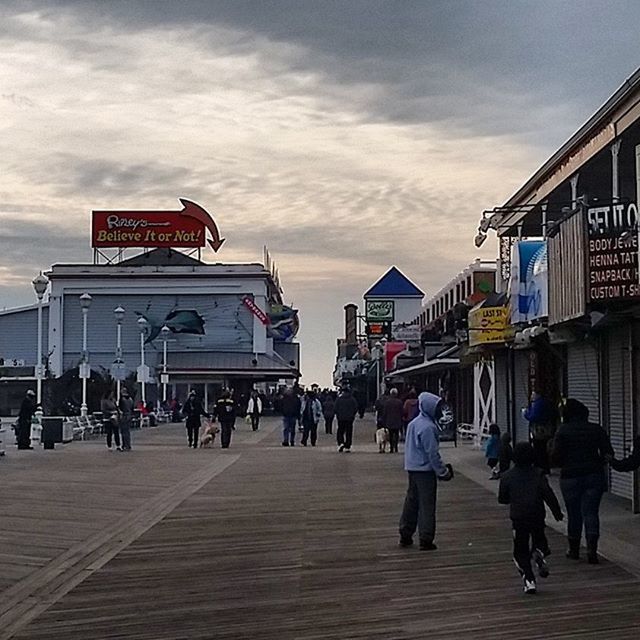 architecture, built structure, building exterior, sky, men, large group of people, person, walking, text, cloud - sky, lifestyles, city, street, city life, western script, leisure activity, transportation, cloud, cloudy