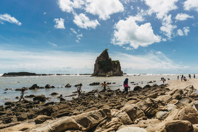 People on rocks by sea against sky