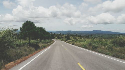 Empty road amidst field against cloudy sky during sunny day