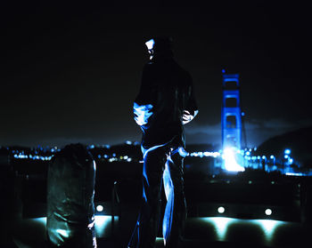 Rear view of silhouette man at illuminated city against sky at night