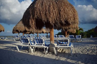 Empty chairs on beach against sky