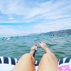 Low section of woman relaxing over inflatable raft on sea against sky