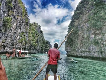 Rear view of man standing on boat in sea amidst rocky cliffs at el nido