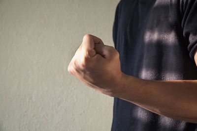 Midsection of man showing fist against wall
